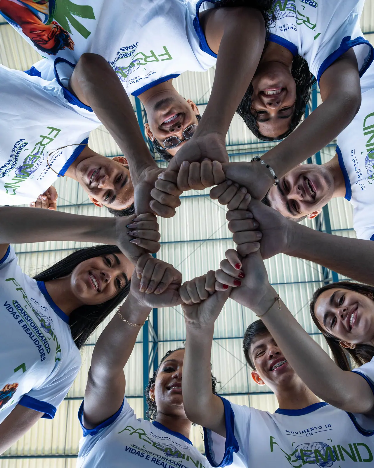 Estudantes do FreeMind, de camisa branca, com as mãos unidas em círculo, vistos de baixo para cima